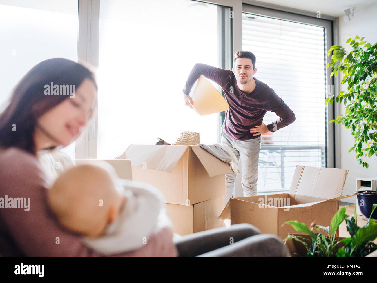 A portrait of young couple with a baby and cardboard boxes moving in a new home. Stock Photo