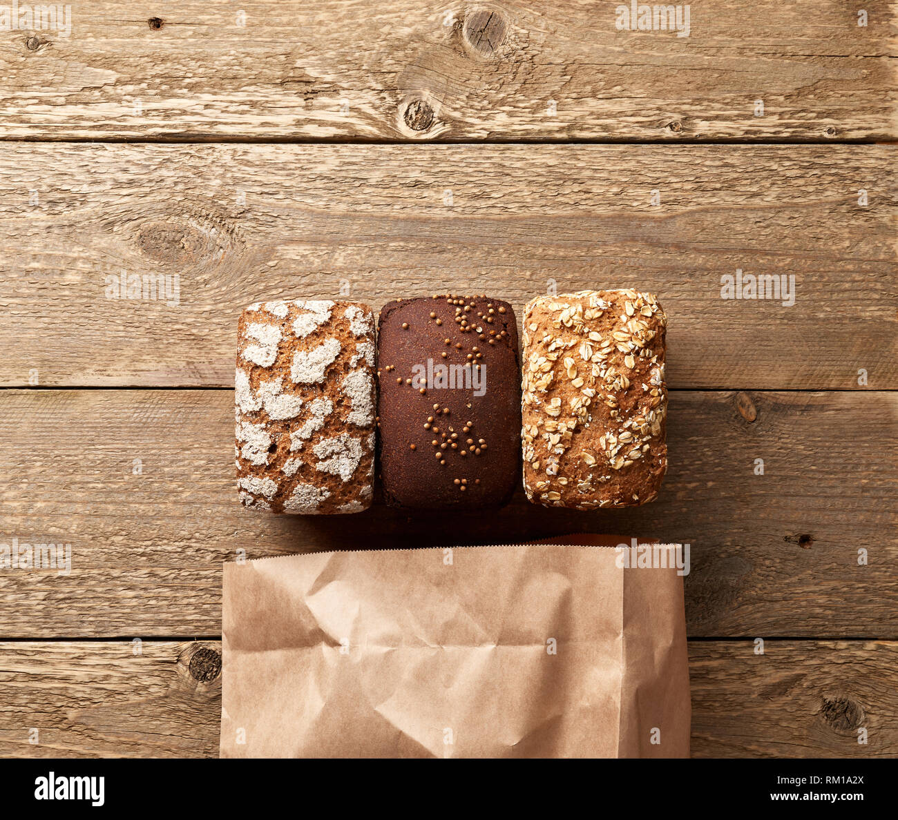 Three loaves of bread on wooden table with paper package. Bakery concept with empty space for design. Gluten-free rye bread with bran and coriander Stock Photo