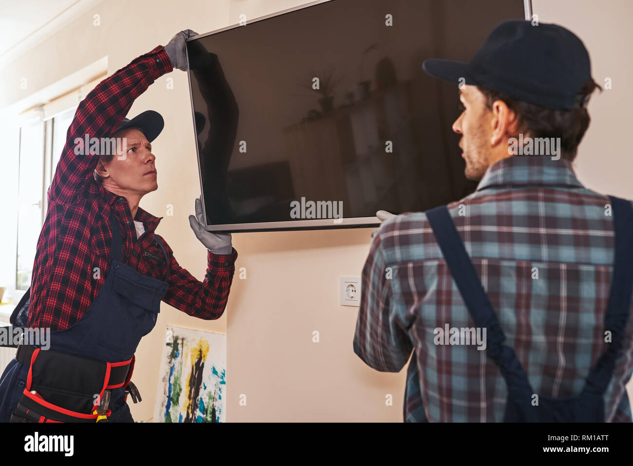 Setting plasma television. Two technician installing television in kitchen of customer. Senior mechanic with young trainee Stock Photo