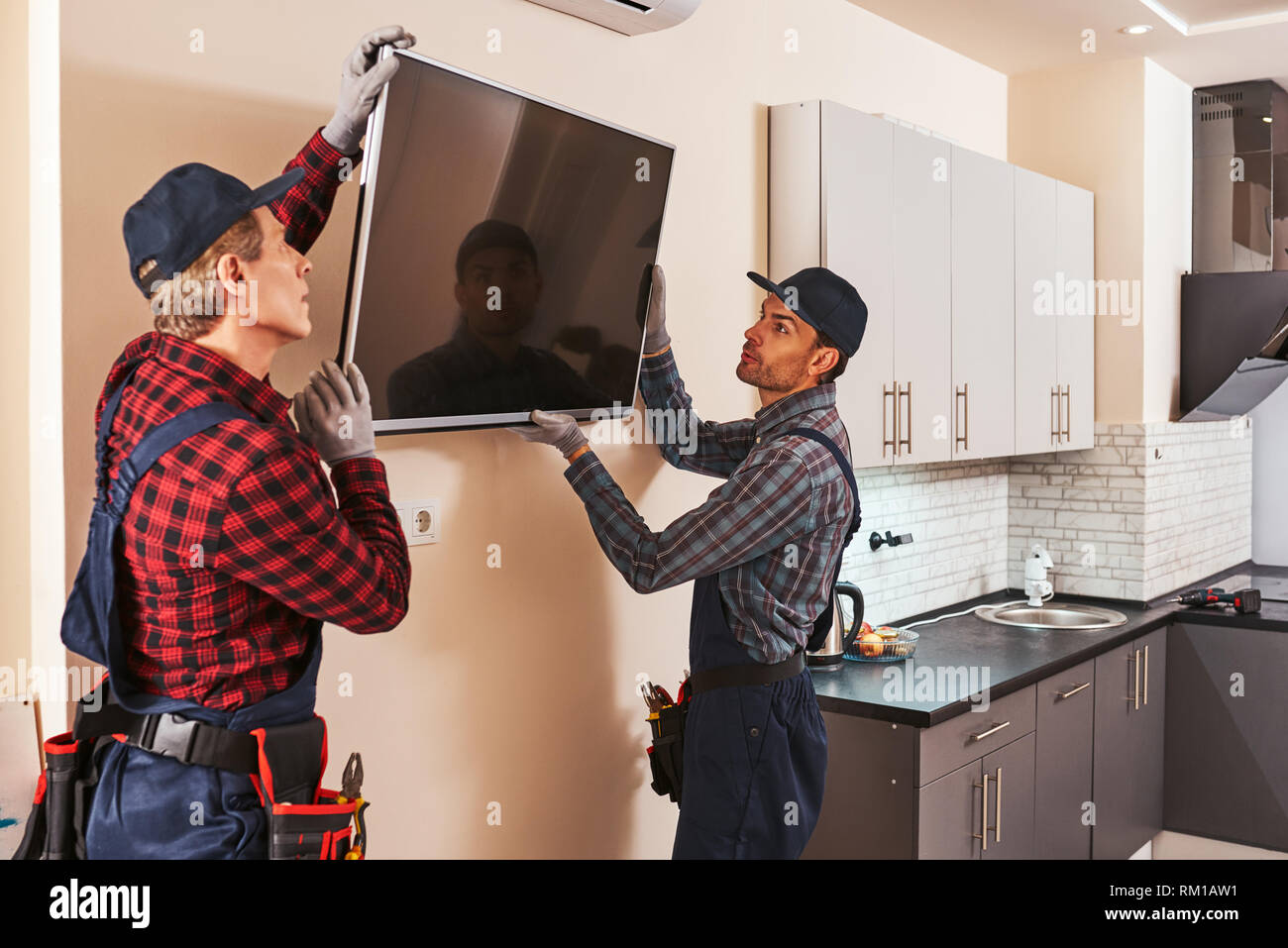 Dismantling of electronics equipment. Two technician remove plasma television in kitchen of customer. Senior mechanic with young trainee Stock Photo