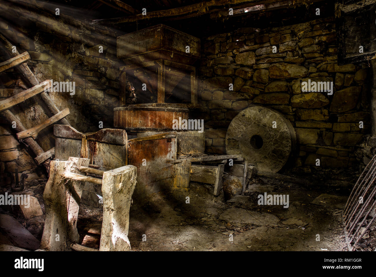 sun rays that pass through the cracks on the roof, and illuminate interiors of old water mill, large circular stone, ladders and etc., long out of use. Stock Photo
