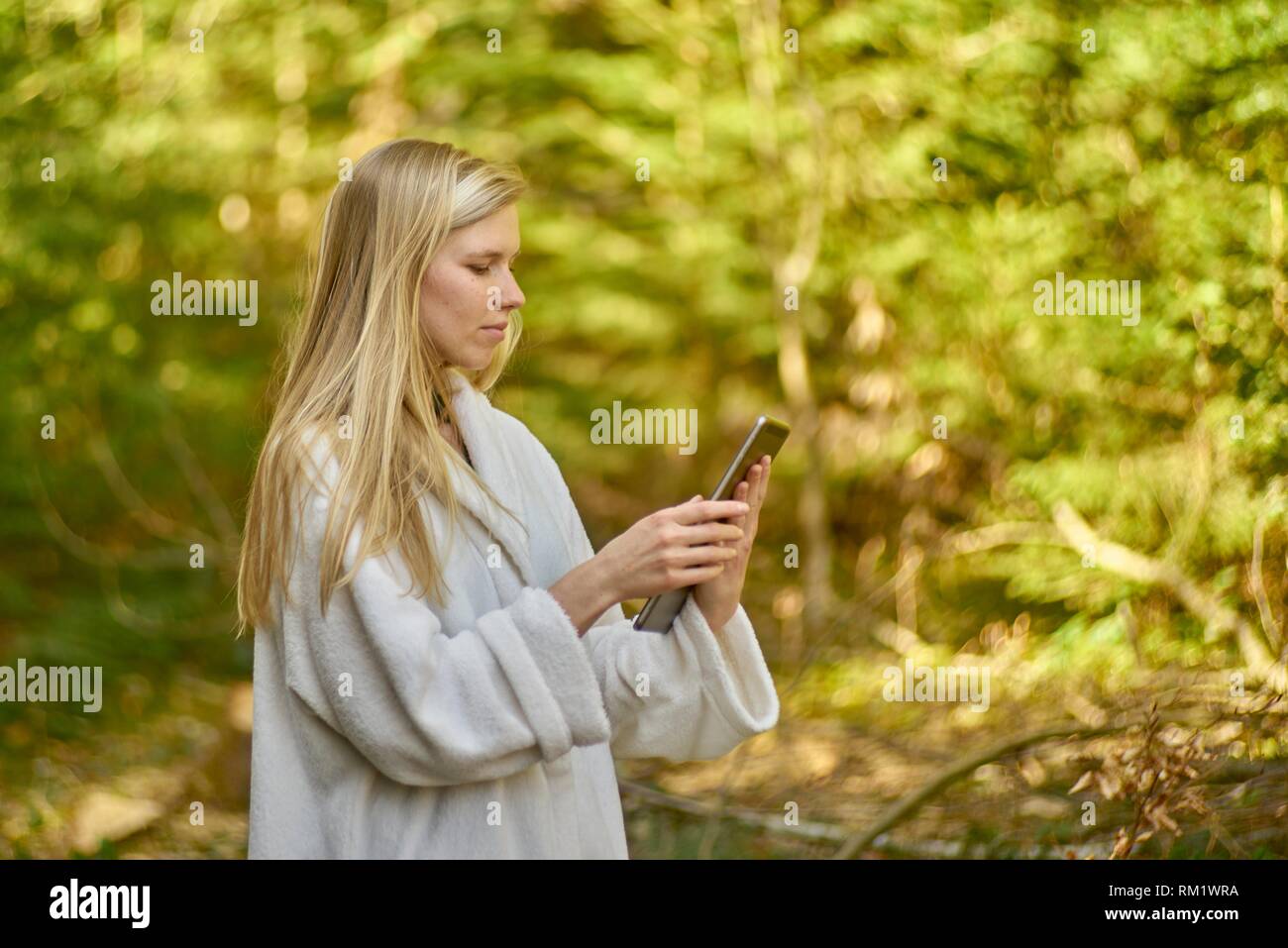 Woman in nature wearing a white bathrobe, using digital table. Waakirchen, Bavaria, Germany