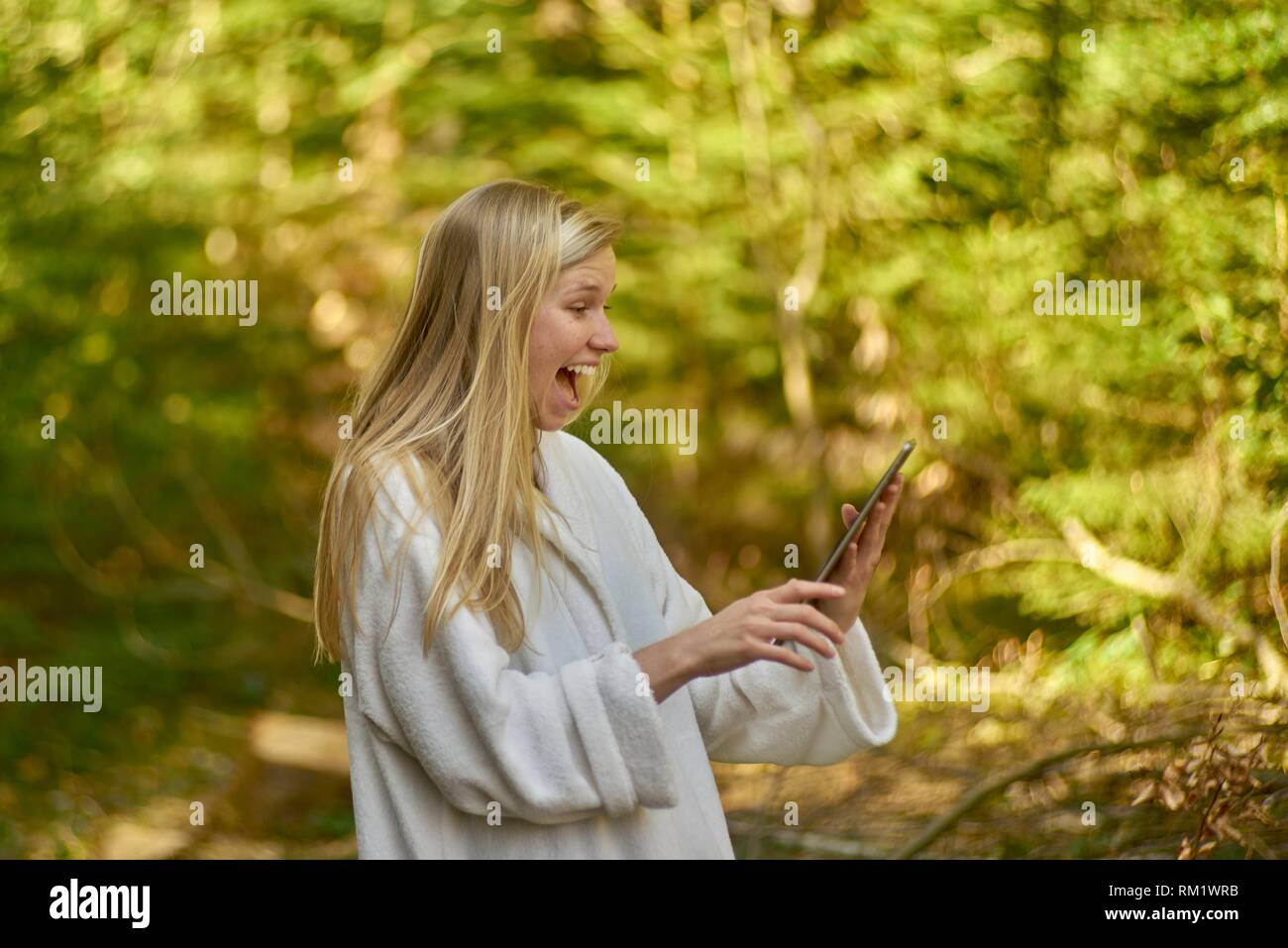 Woman in nature wearing a white bathrobe, using digital table. Waakirchen, Bavaria, Germany