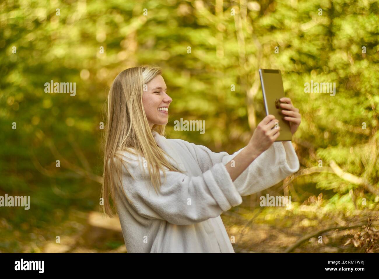 Woman in nature wearing a white bathrobe, using digital table. Waakirchen, Bavaria, Germany