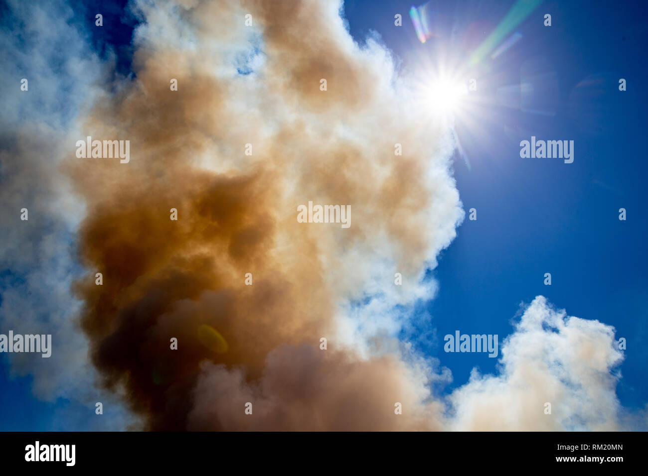 The dramatic smoke from a stubble fire on a farm billows up towards the afternoon sun in the sky Stock Photo