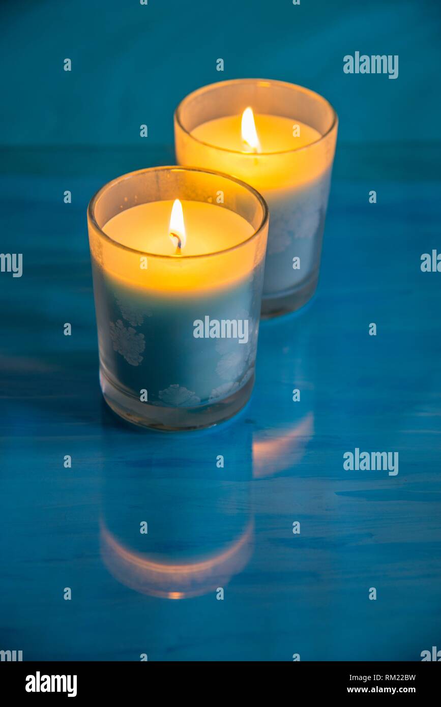 Two lit up candles on blue surface. Stock Photo