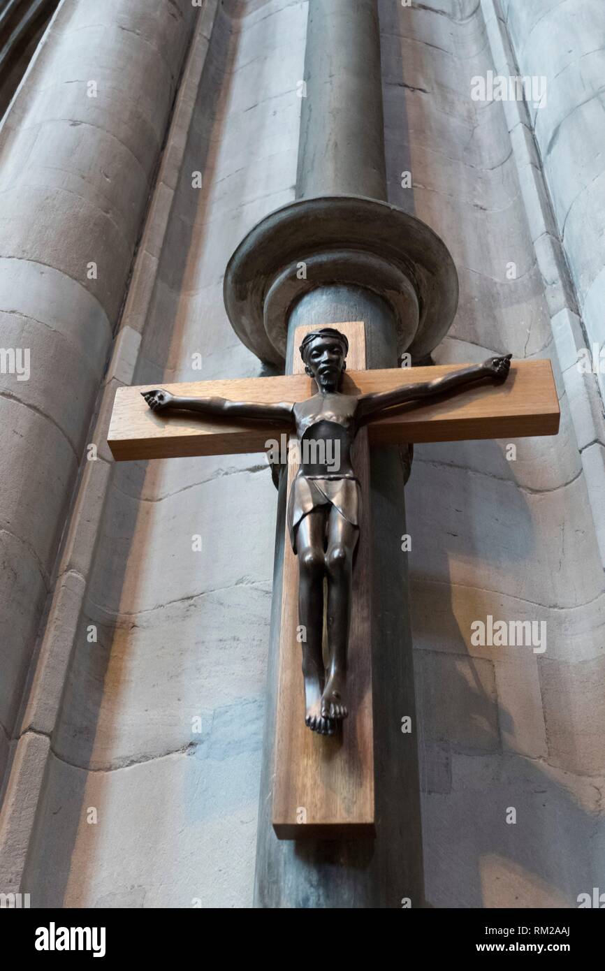 Bronze crucifix of a negro Christ outstretched on a wooden cross hung from a carved stone column in Hereford Cathedral, Hereford, England. Stock Photo