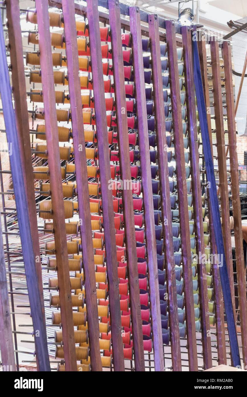 Racks of repeating rainbow coloured threads on wooden reels in traditional jacquard weaving industry, La Manufacture de Roubaix, France. Stock Photo