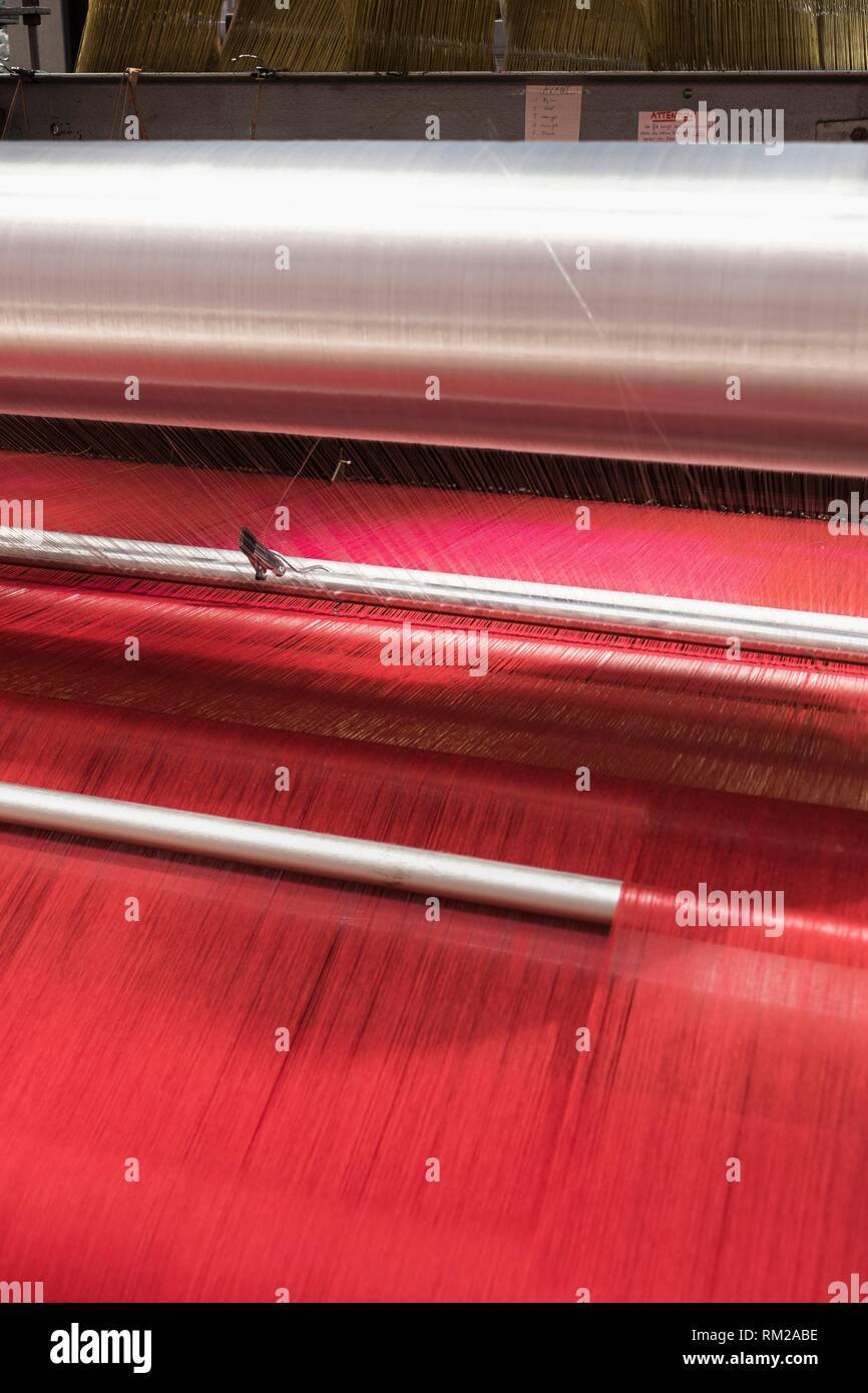 Hot pink threads cascade through reflective metallic cylinders on a jacquard farbic loom, La Manufacture de Roubaix, France. Stock Photo