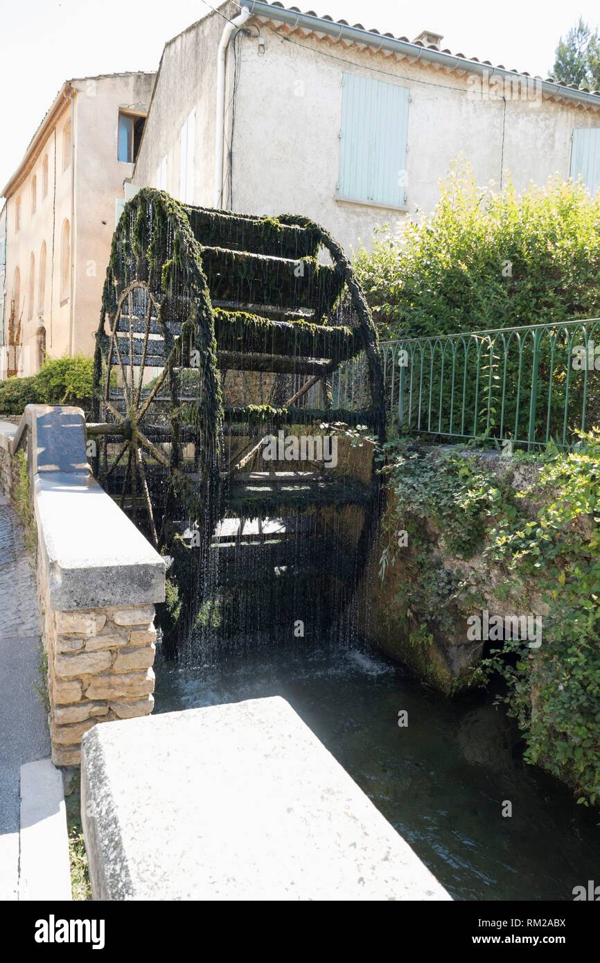 Moss covered waterwheel with shimmering beads of clear water cascading into the transparent waters of the river Sorgue in L'Isle-sur-la-Sorgue, Stock Photo