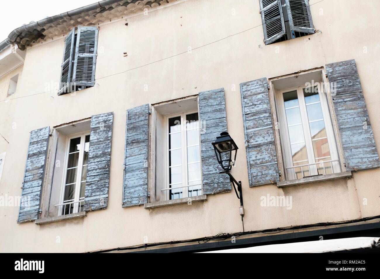 Sun weathered, pale blue rustic shutters on a traditional Provencal house with carriage lamp in L'Isle-sur-la-Sorgue, Provence, France. Stock Photo