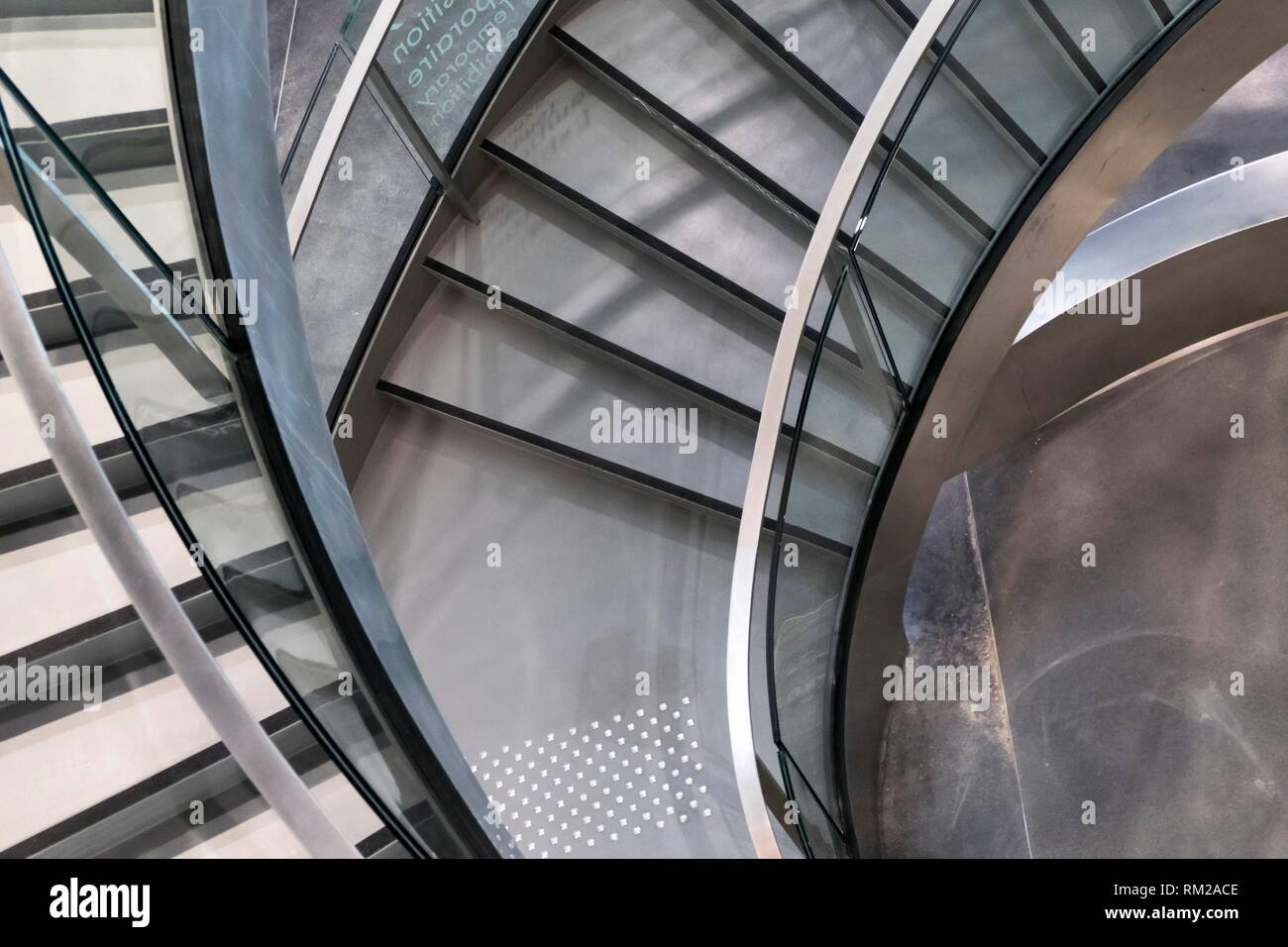 Curving fan of chrome, black and silver stairs spiralling to a vortex with textured flooring at the Roman Museum, Nimes, France. Stock Photo