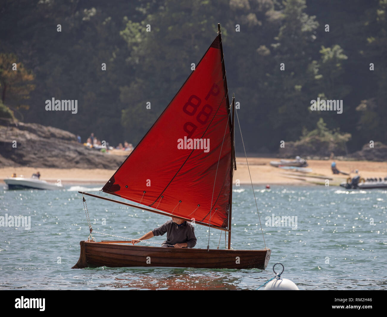 The small boat with a red sail enjoying the Salcombe Estuary. Stock Photo