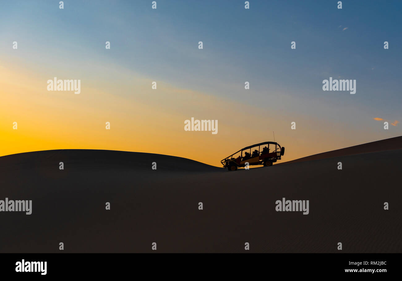 The silhouette of a sand dune and buggy in the Peruvian desert of Ica near the Huacachina Lagoon at sunset in Peru. Stock Photo