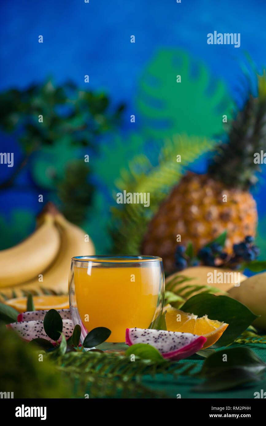 Tropical fruits fresh juice on a blue background with bananas, pineapple, mango and dragon fruit. Exotic drink concept with copy space Stock Photo