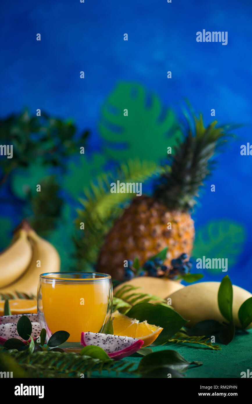Tropical fruits fresh juice on a blue background with bananas, pineapple, mango and dragon fruit. Exotic drink concept with copy space Stock Photo