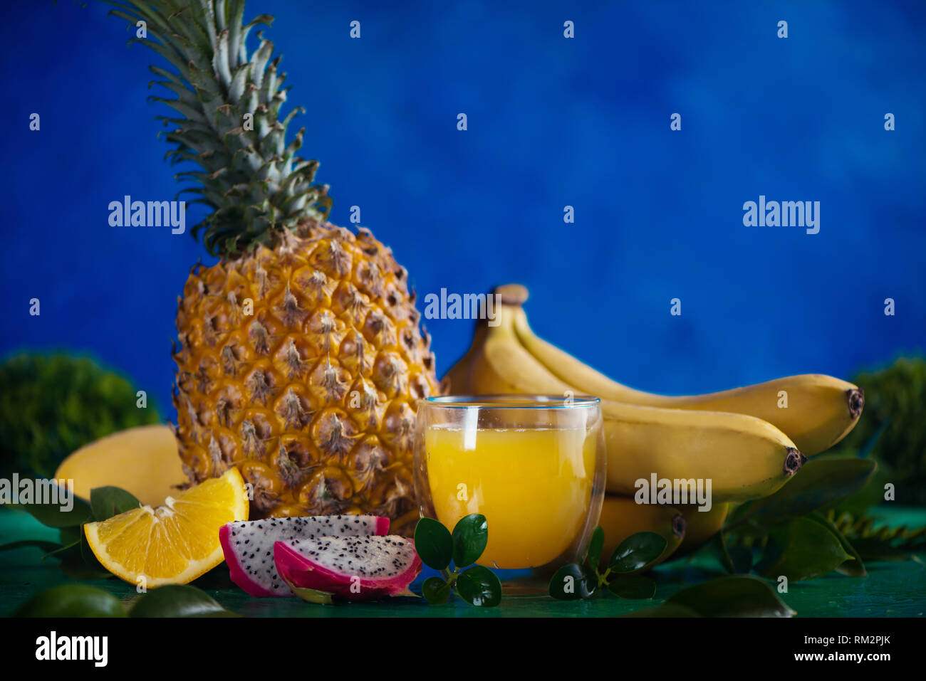 Tropical fruits fresh juice on a blue background with bananas, pineapple, mango and dragon fruit. Exotic drink header with copy space Stock Photo