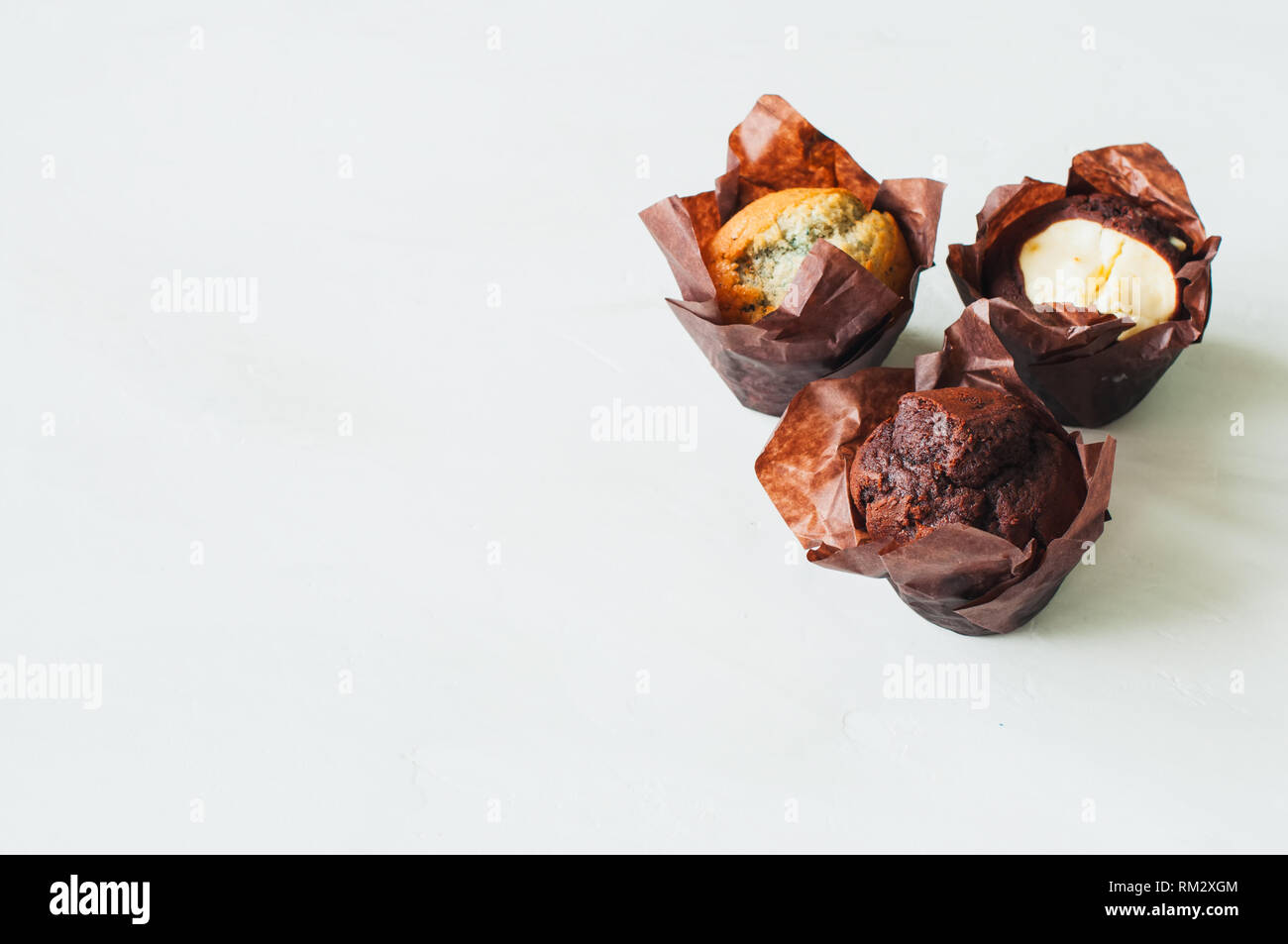 Three different muffins on a white background. Chocolate, bluberry and brownie cheesecake muffins. Copy space. Stock Photo