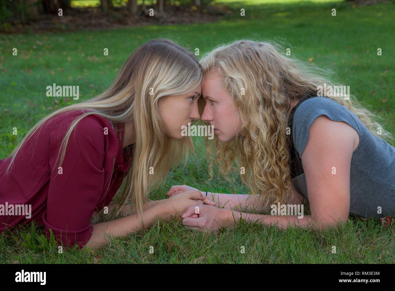 Two blonde teenage girls lying on the grass head-to-head. Stock Photo