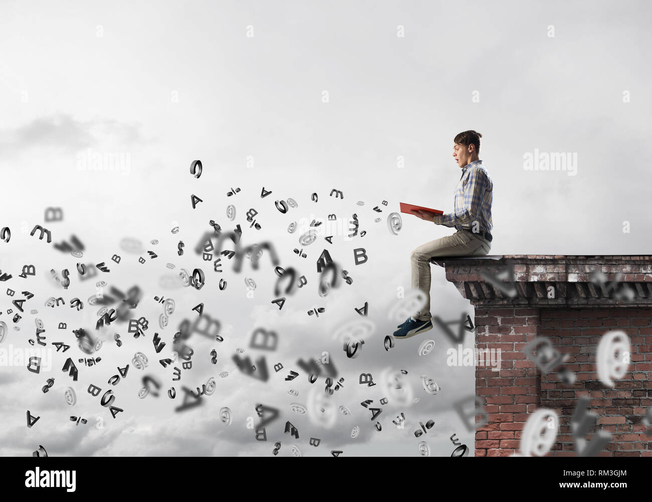 Man on roof edge reading book and symbols flying around Stock Photo
