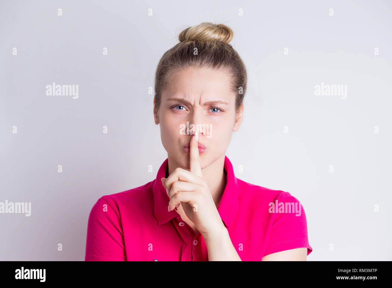 Beautiful young female in pink dress demonstrates silence gesture, keeps forefinger on lips on white background. Body language concept Stock Photo