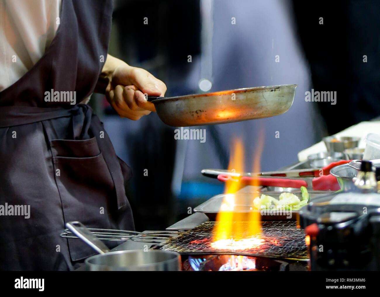 Chef cooking with flame in a frying pan on a kitchen stove, Chef in ...