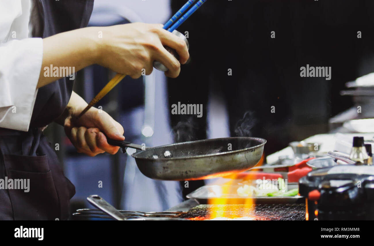 Chef cooking with flame in a frying pan on a kitchen stove, Chef in ...