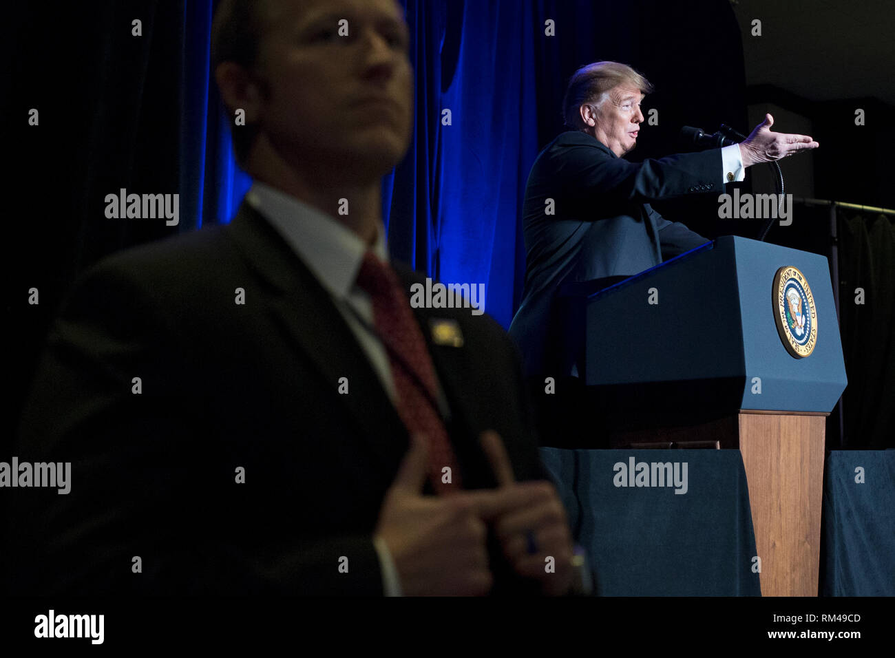 US President Donald J. Trump (R) is seen behind a US Secret Service agent delivering remarks at the Major County Sheriffs and Major Cities Chiefs Association Joint Conference, in Washington, DC, USA, 13 February 2019. Trump took the opportunity to deliver remarks on his border-security and immigration policy. Republican leaders are asking Trump to sign legislation that allocates about 1.375 billion USD (1.218 billion euros) for over fifty miles of physical barriers along the border. Signing the agreement would prevent another partial shutdown of the federal government that would begin 16 Febru Stock Photo