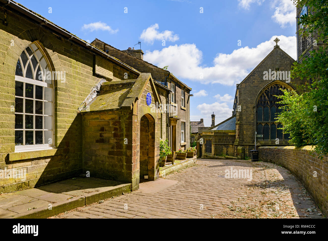 Exterior of sunlit historic Old School Room (Brontes taught here) cobbled lane & St Michael & All Angels Church - Haworth, West Yorkshire, England, UK Stock Photo