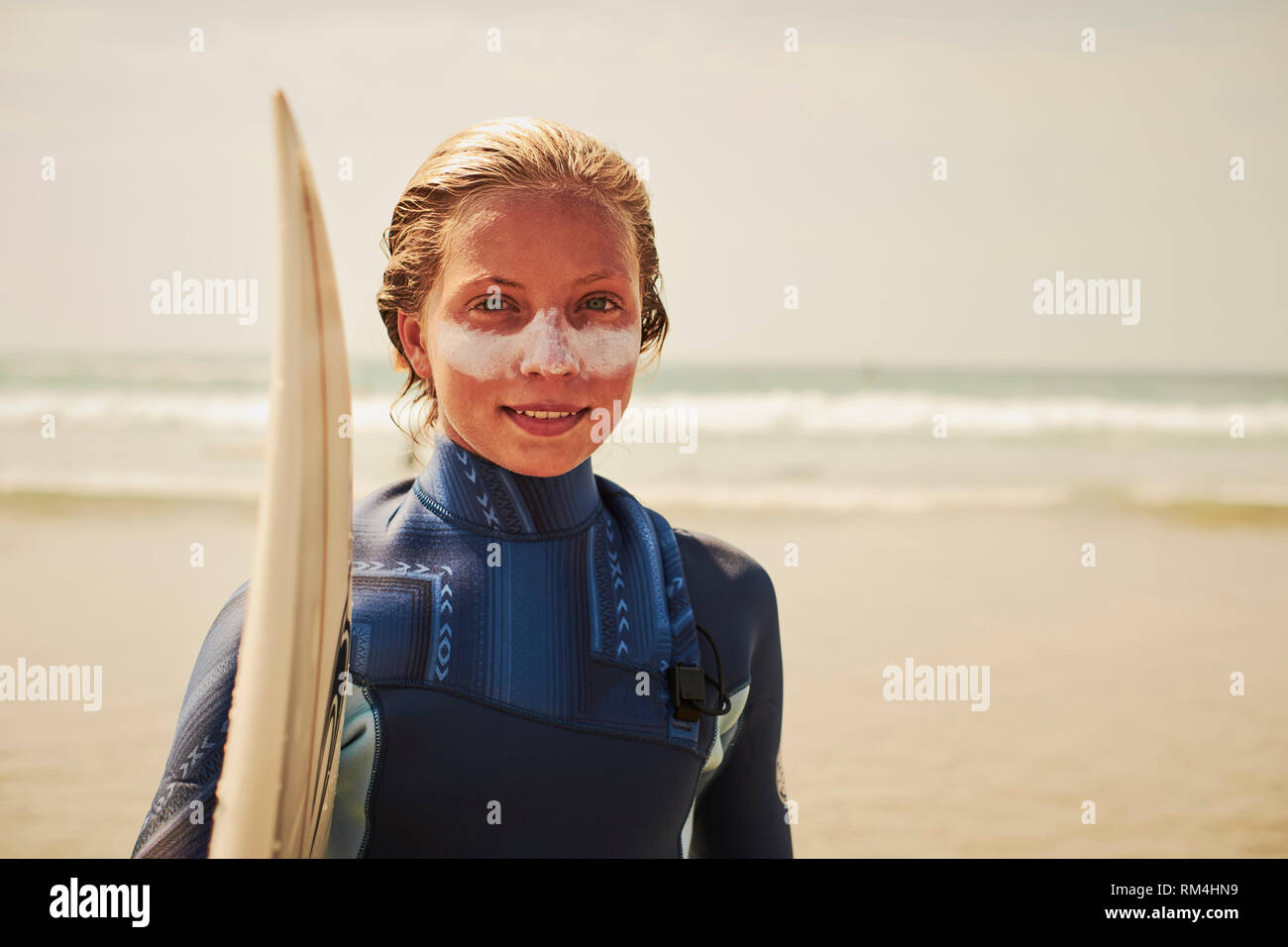 An outdoor lifestyle portrait of a teenage young girl surfer with her surfboard and sun cream protection on the beach - lifestyles watersports Stock Photo