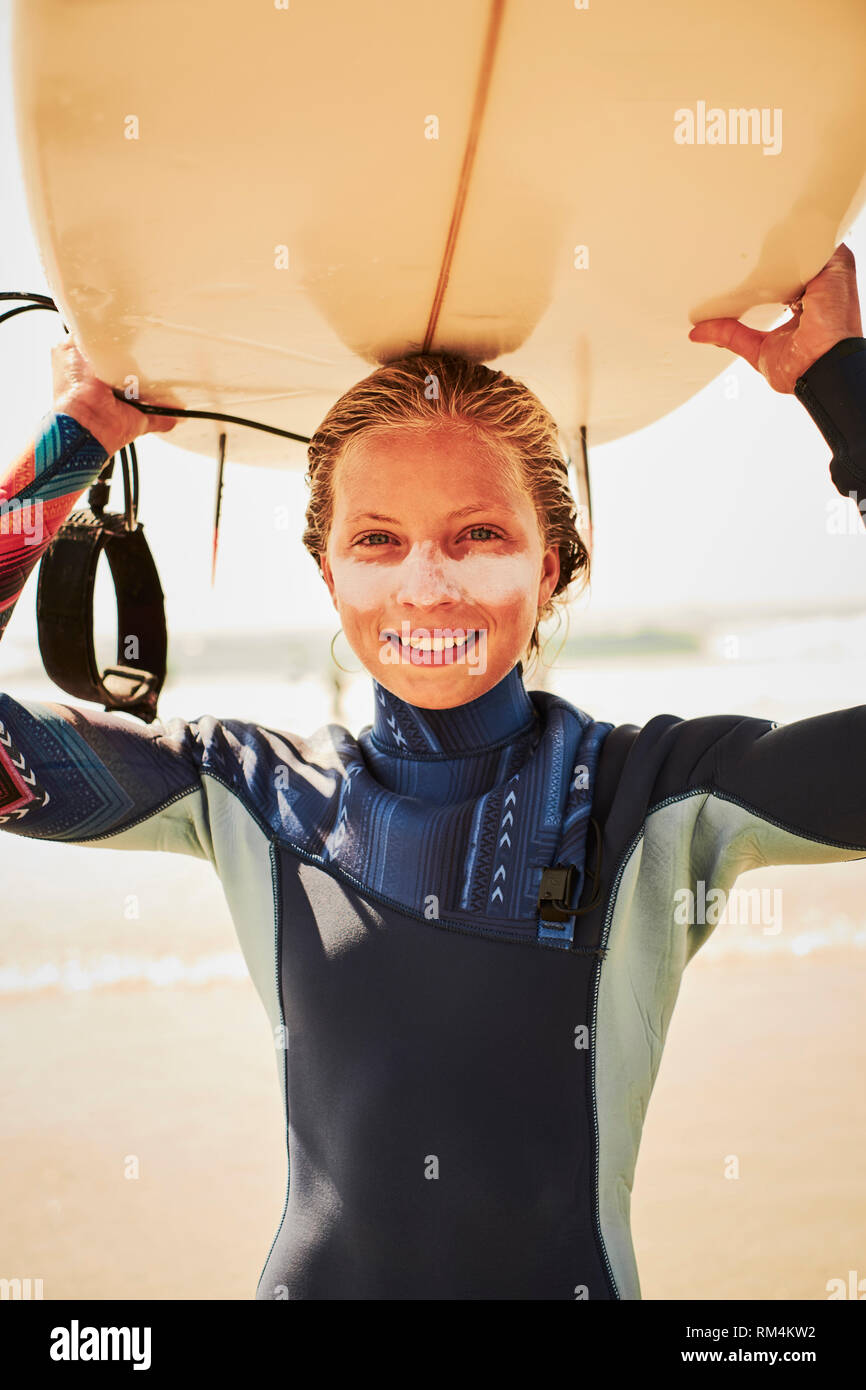 An outdoor lifestyle portrait of a teenage young girl surfer with her surfboard and sun cream protection on the beach - lifestyles watersports Stock Photo