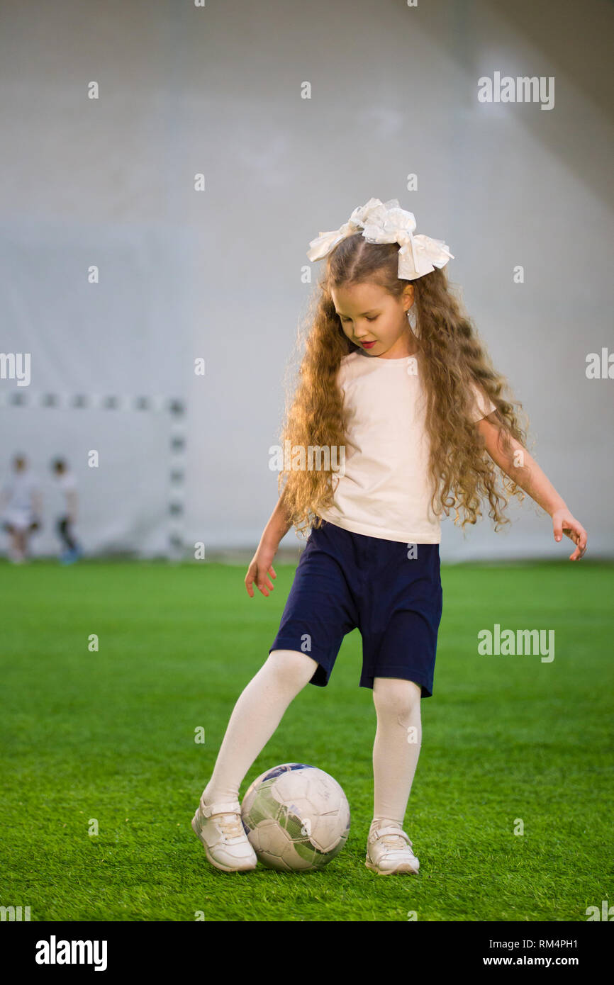 A little girl kicking the ball on the football field playing the game