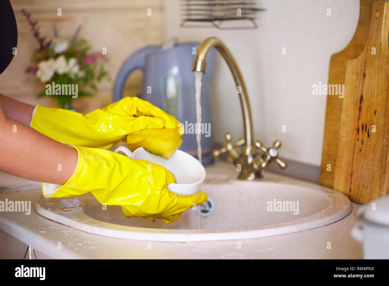 Close up hands of woman wearing yellow gloves washing dishes in kitchen