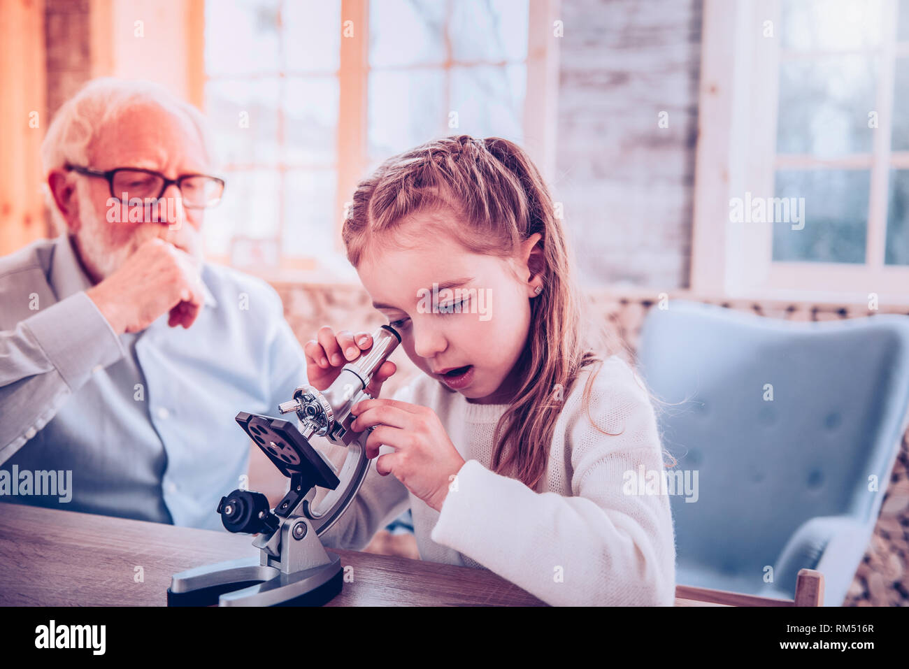 Smart schooler with nice hairstyle using microscope Stock Photo