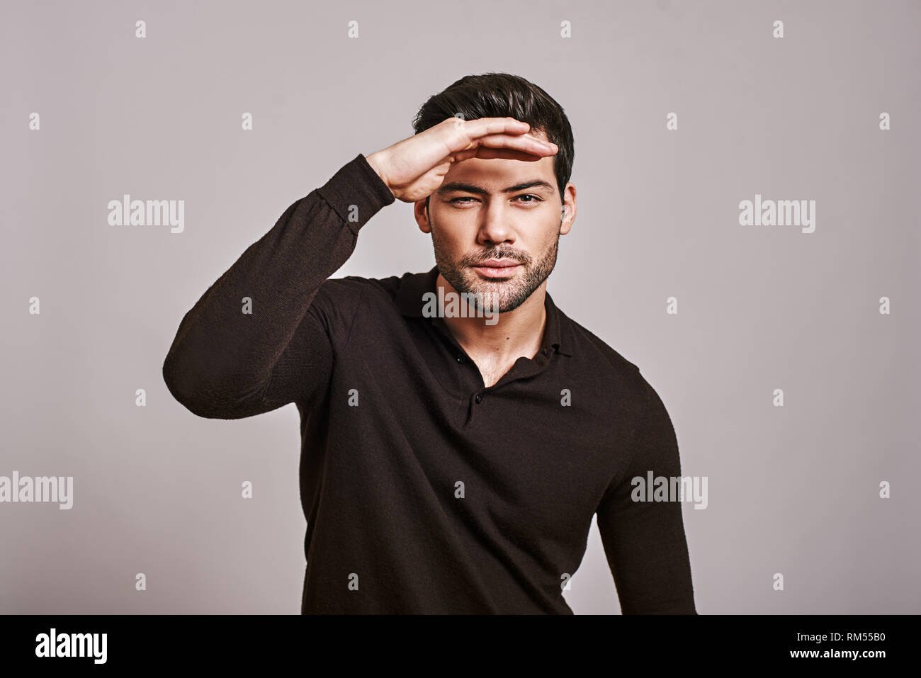 Closeup portrait of young serious curious squinting man, hand on head, peering ahead, searching for something, looking to the future at camera, isolated over white background. Sign, symbols Stock Photo