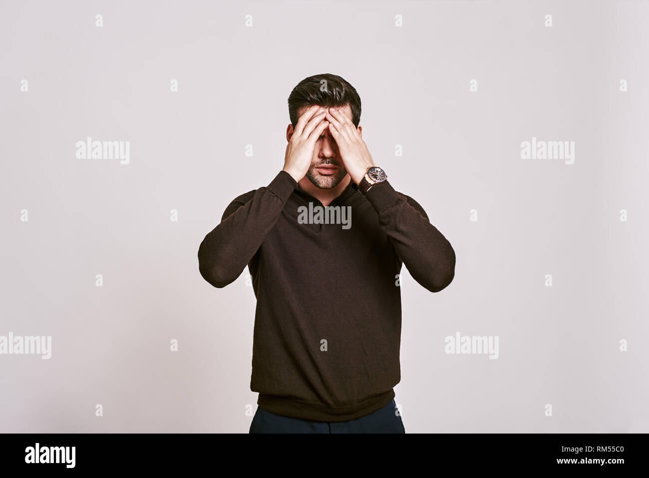 Handsome young man in brown jumper touching his head with hand feeling strong headache. Office manager is tired and exhausted after long working day Stock Photo