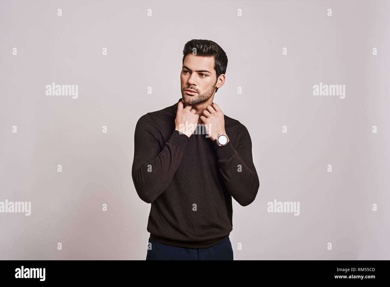 Photo of attractive serious man dressed in brown jumper posing over grey background. Looking aside. Stock Photo