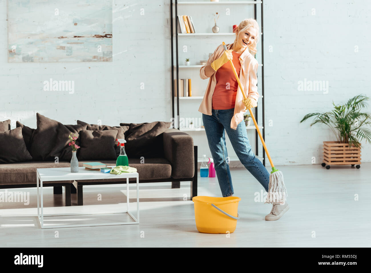 Laughing senior woman dancing while cleaning floor with mop Stock Photo