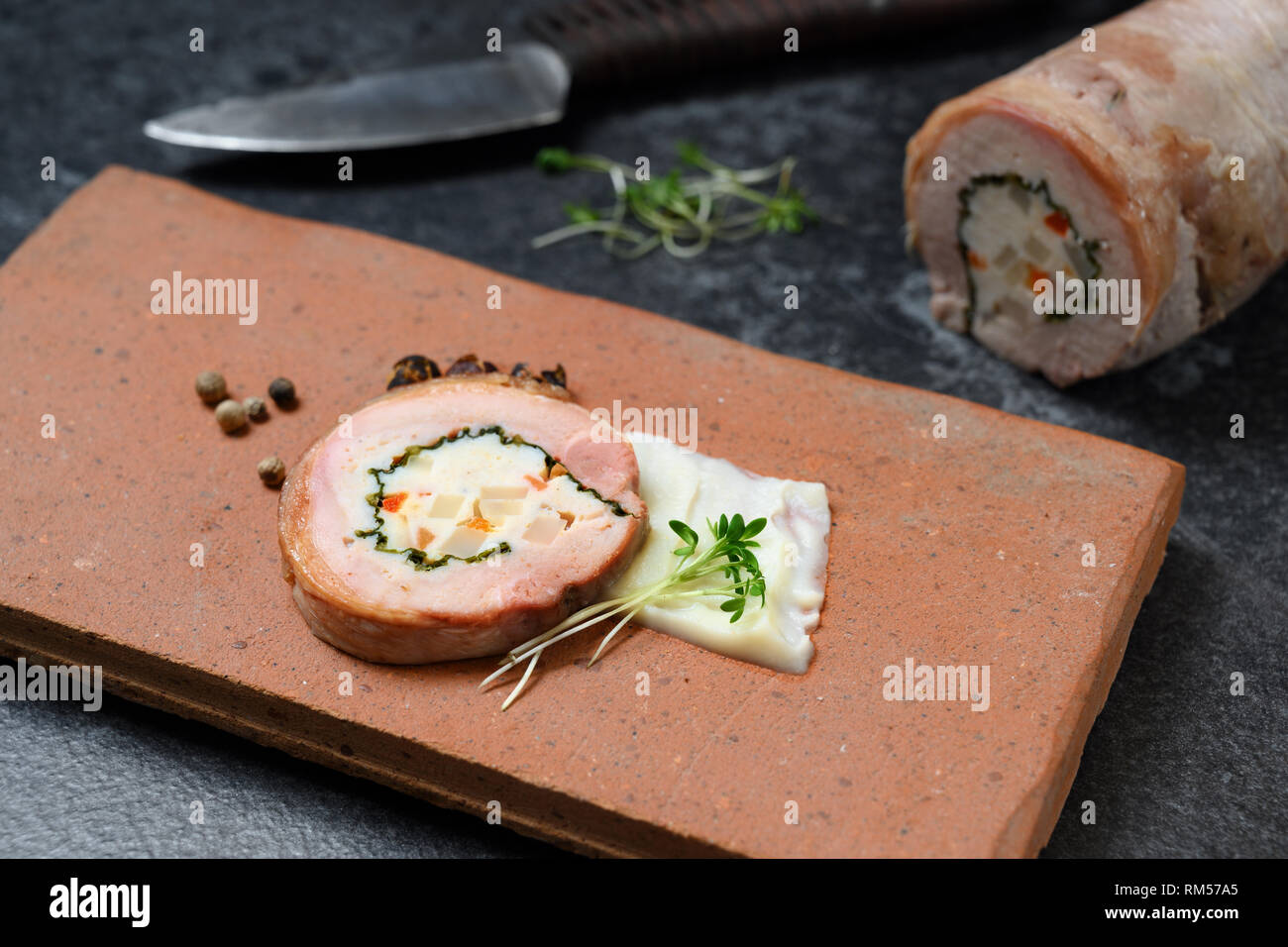 quail galantine, de-boned stuffed meat for a festive dinner served on a rustic brick plate on a dark table, copy space, selected focus, narrow depth o Stock Photo