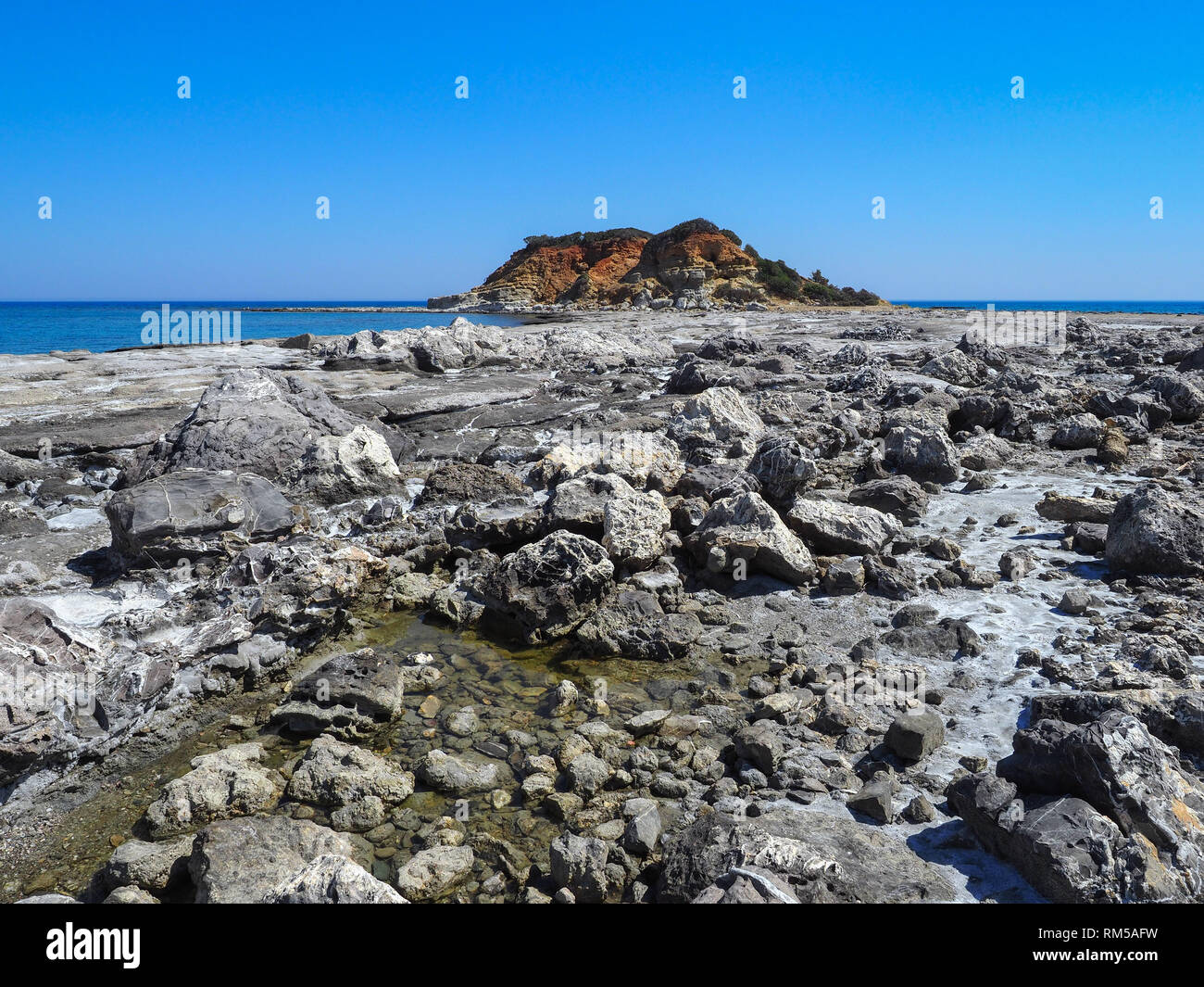 Wonderful beauty wild beach with stony rocky shore and in the distance visible colorful hill near the Kiotari, Rhodes Island, Greece.Beautiful scenery Stock Photo