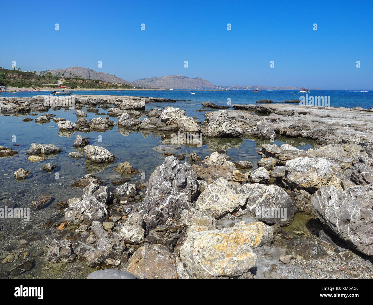Wonderful beauty wild beach with stony rocky shore, shallow sea water. Beautiful scenery and sunny day on Kiotari, Rhodes Island, Greece. Stock Photo
