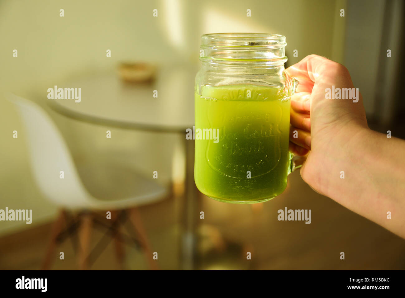 Woman hand holding Celery Healthy Green Juice in jar at sunny morning kitchen Stock Photo