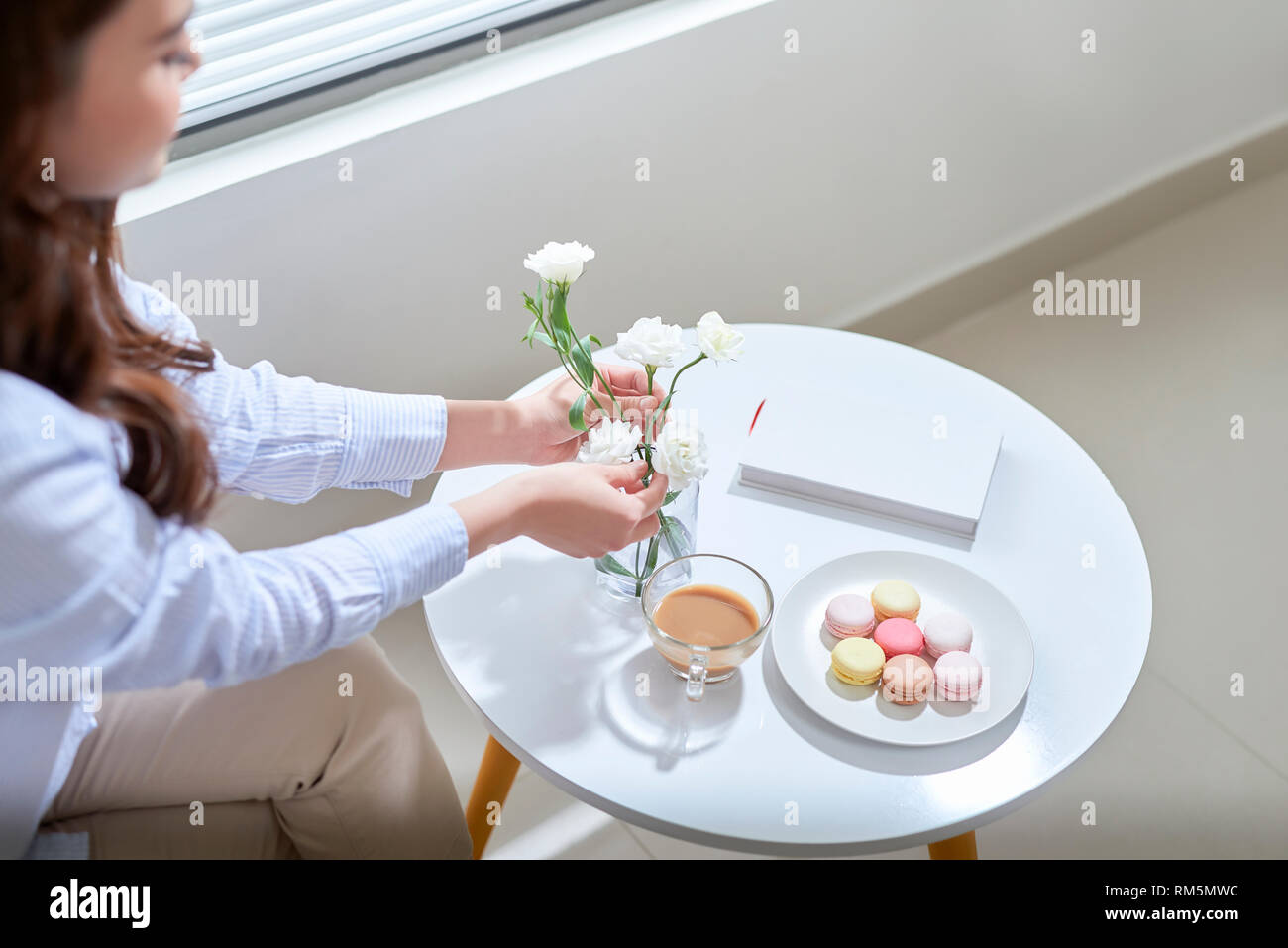 Woman arranging lisianthus flowers in a glass vase at home. Stock Photo