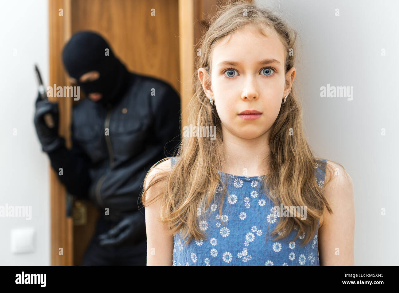 Shocked little girl and angry robber with gun in the background. Stock Photo
