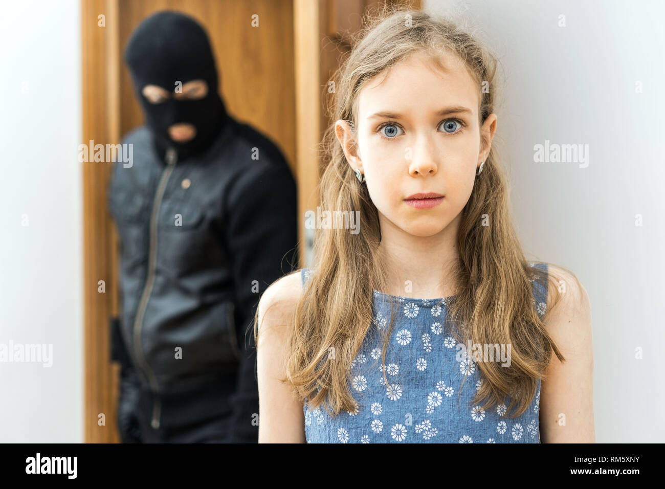Shocked little girl and angry robber in the background. Stock Photo