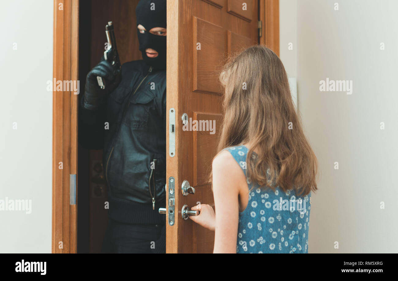 Little girl opening the door to the robber with gun. Stock Photo