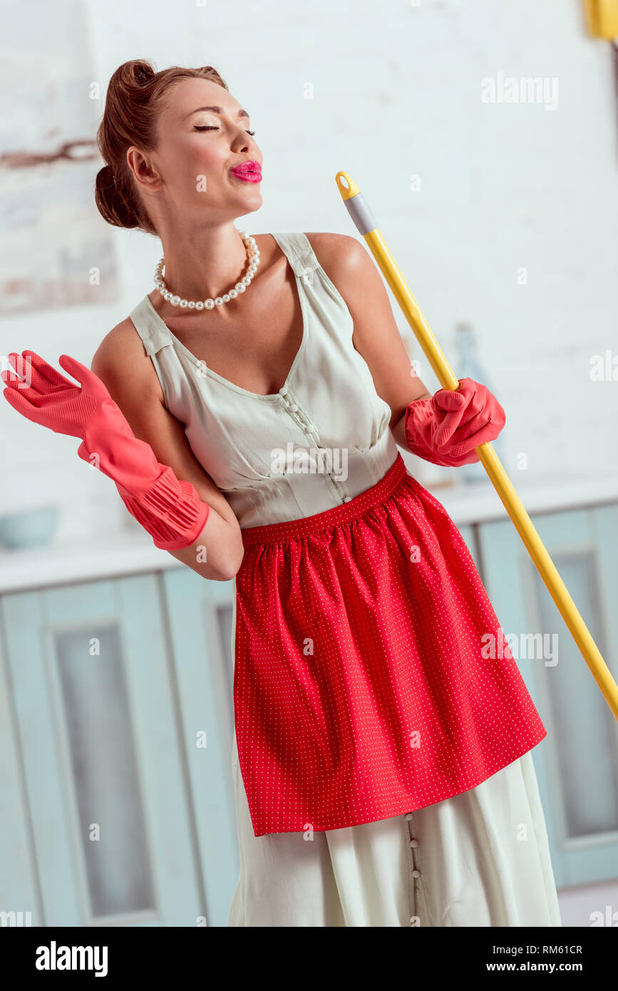 Pretty pin up girl waving hand and making duck face while holding yellow mop Stock Photo