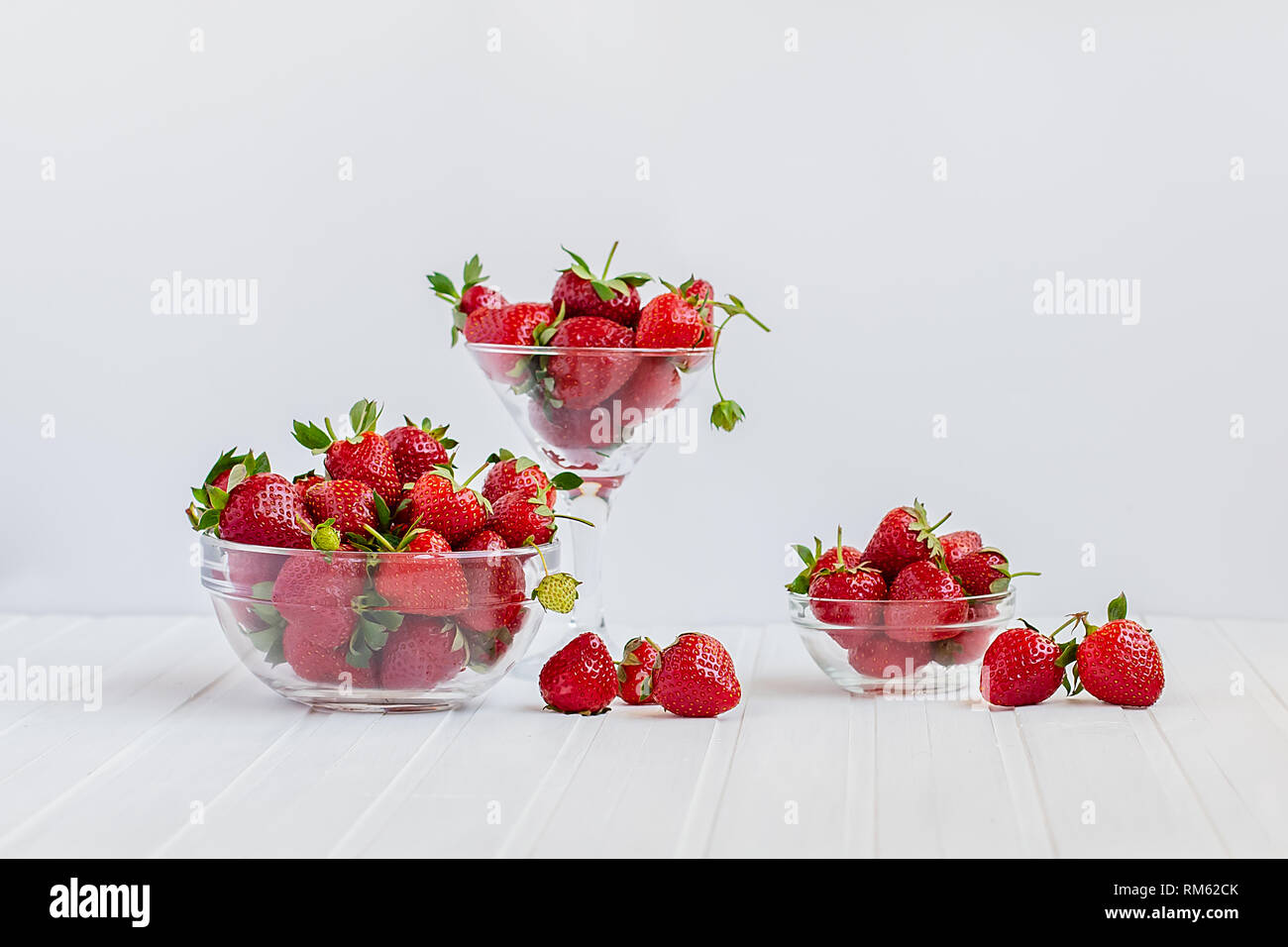 Red ripe strawberries in a glass bowl on a white wooden table. Harvest ...
