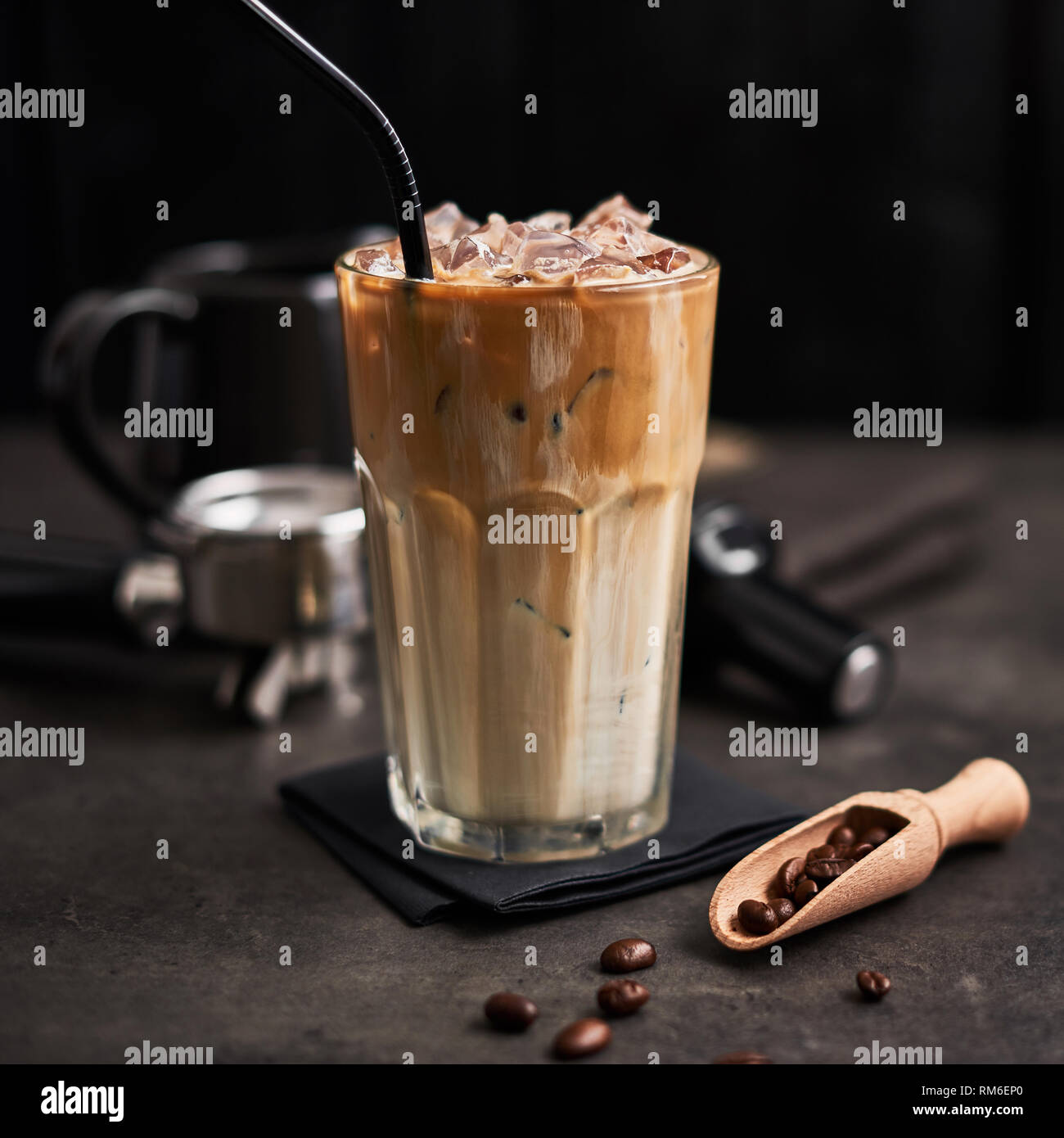 Ice coffee with cream in a tall glass and coffee beans, portafilter, tamper and milk jug on dark concrete table over black wooden background. Cold sum Stock Photo