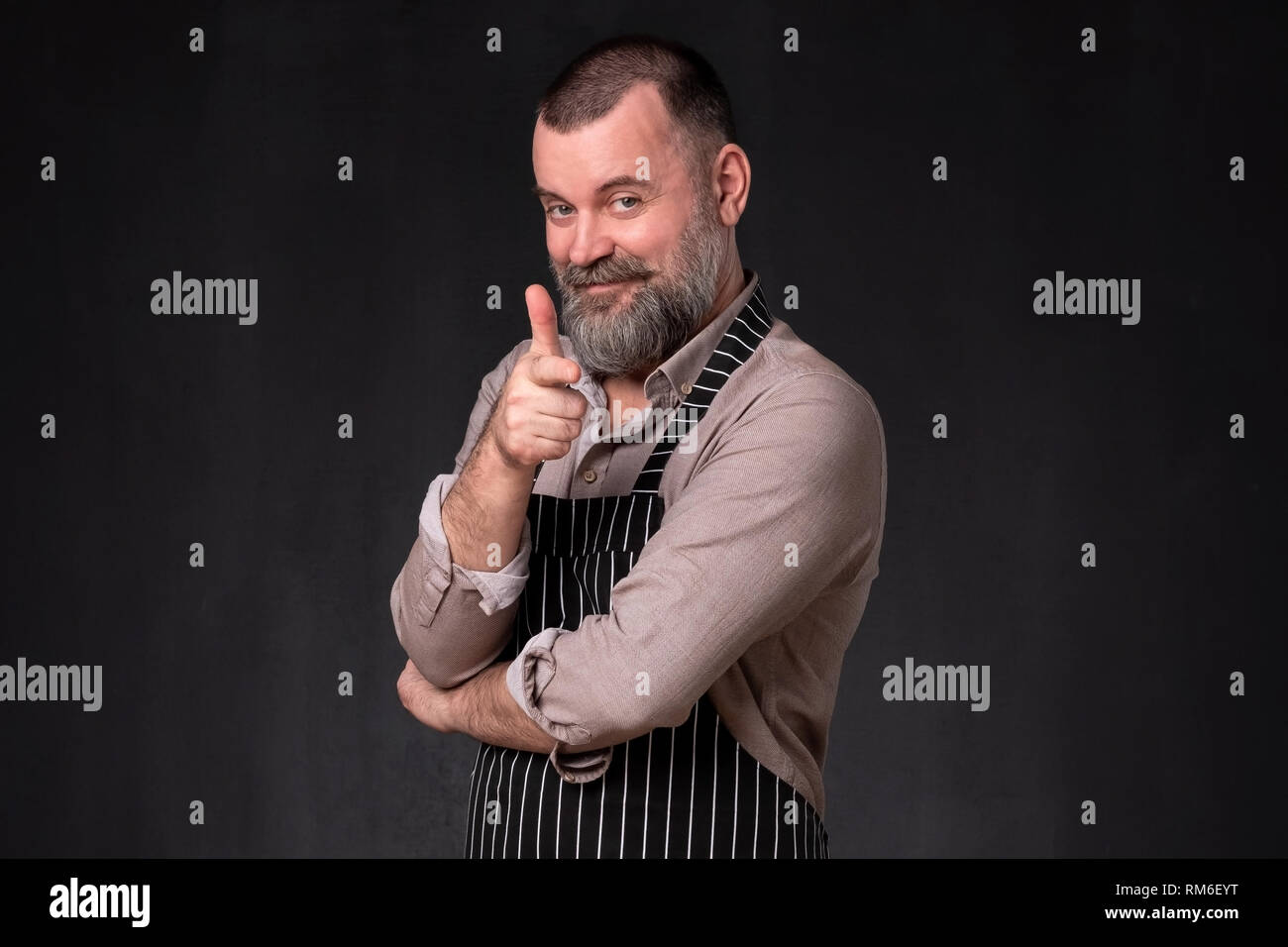 Mature bearded man in apron pointing with finger at camera Stock Photo
